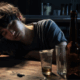 An asian looking young gay man, seemingly drunk in a table with glasses and bottles of alcohol.