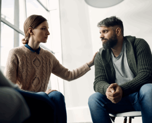 A female therapist comforting a gay person in a trauma-informed addiction treatment center.