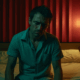 A gay man sitting on the edge of a bed in room admitting he has an addiction problem.