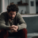 Gay man sitting alone on a couch appearing overwhelmed because of addiction.
