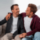 One gay man comforting another gay man in a gay sober living sitting on a couch.
