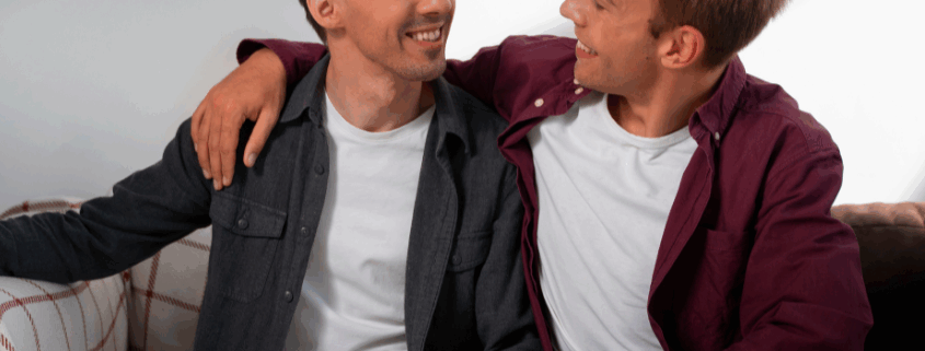 One gay man comforting another gay man in a gay sober living sitting on a couch.