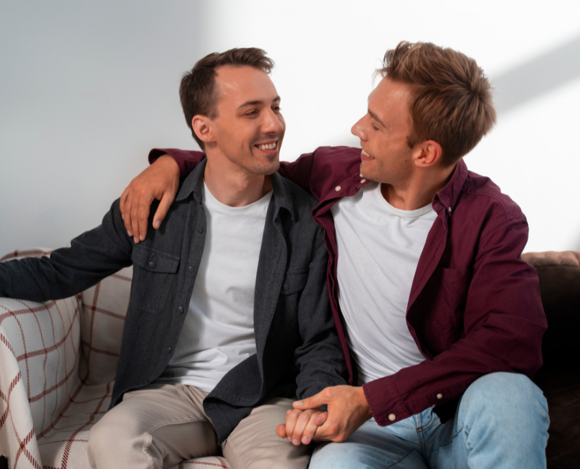 One gay man comforting another gay man in a gay sober living sitting on a couch.