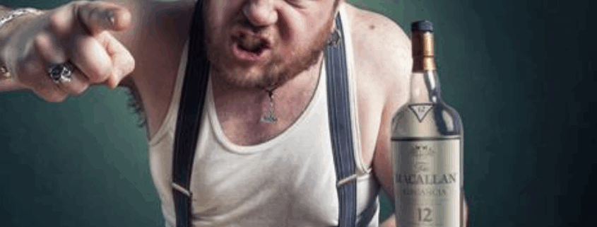A raging alcoholic yelling while pointing, holding a glass of whiskey next to a bottle.