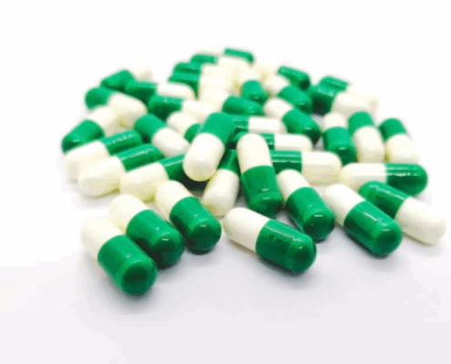 Green-white tramadol capsules scattered on a white surface.