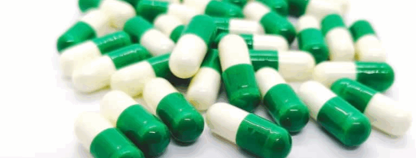 Green-white tramadol capsules scattered on a white surface.