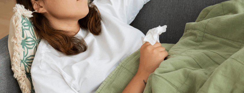 A lesbian woman lying on a couch holding a tissue and looking unwell from klonopin withdrawal.