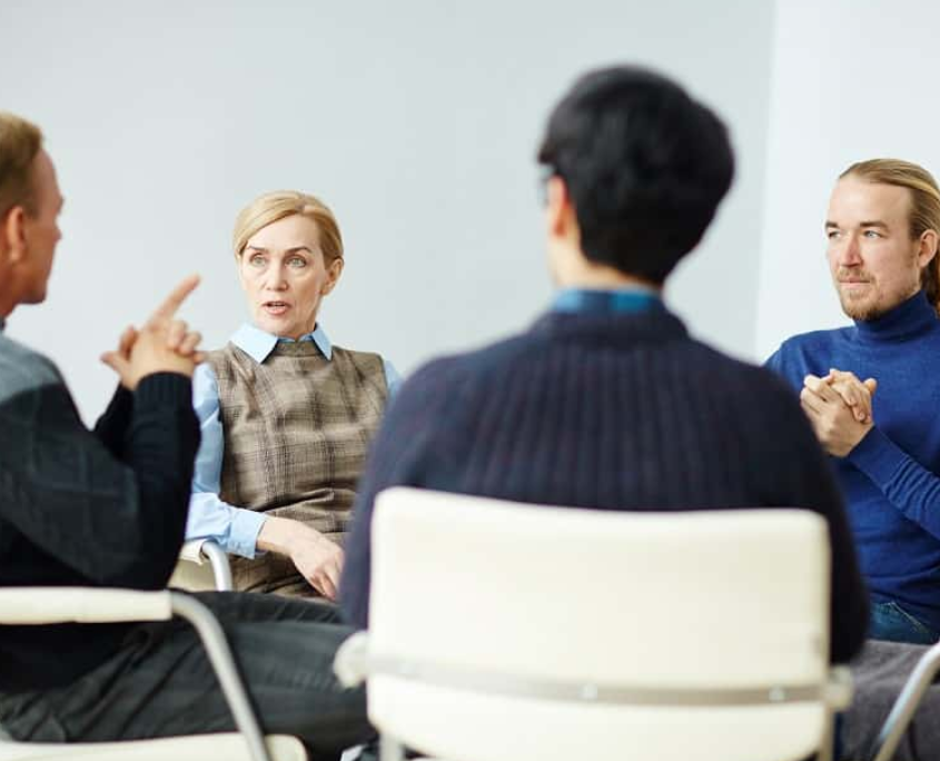 A small group of people at a beginners NA meeting all looking at the person speaking.