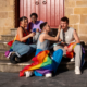 A group of LGBTQ individuals draped in pride flags, enjoying a moment of connection, symbolizing healing societal trauma through community and support.