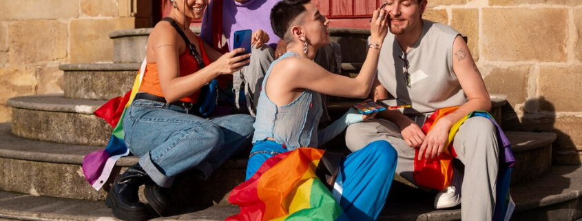 A group of LGBTQ individuals draped in pride flags, enjoying a moment of connection, symbolizing healing societal trauma through community and support.