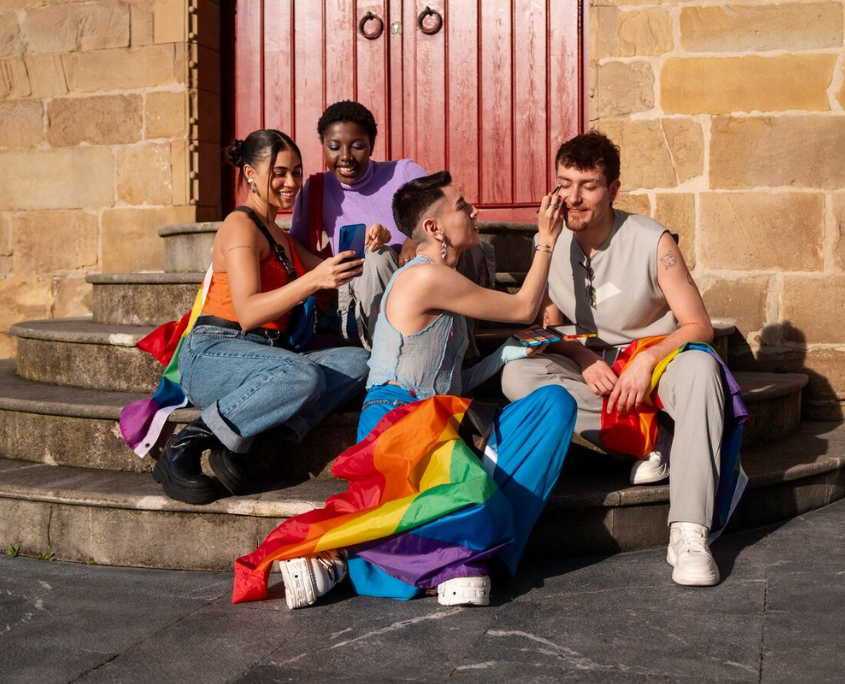 A group of LGBTQ individuals draped in pride flags, enjoying a moment of connection, symbolizing healing societal trauma through community and support.