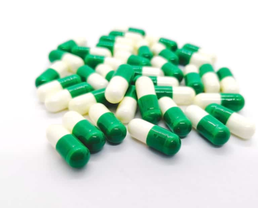 Green-white tramadol capsules scattered on a white surface.
